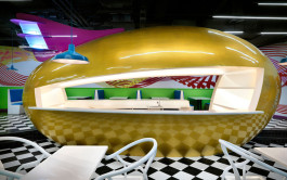 Colorful restaurant interior featuring a central golden egg-shaped volume with a bar counter, designed by Ballistic Architecture Machine. 