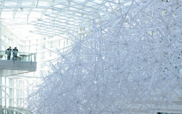 Two people gaze at the 'Wintergarden' installation from a balcony overlooking the atrium. The installation features crisscrossing white tubes that create a complex yet airy structure. 